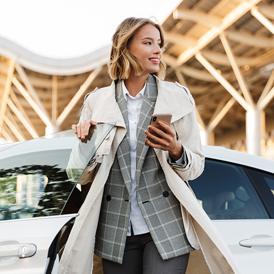 Person mit Smartphone vor einem Mietwagen in moderner Umgebung – Sunny Cars Mietwagen bequem über Kuoni buchen.