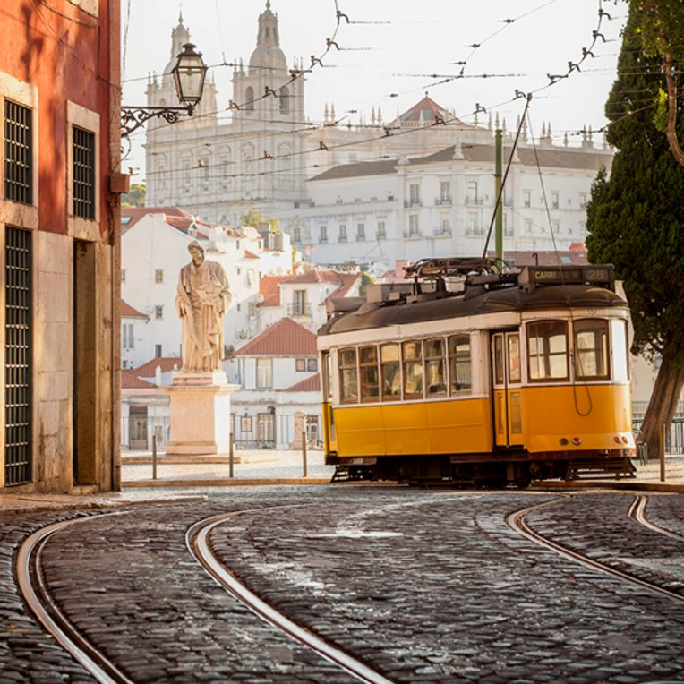 Un tramway jaune et blanc sur une rue pavée à Lisbonne.