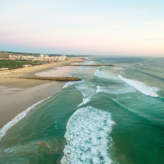 Plage à Lisbonne avec des vagues et un vaste plan d'eau sous un ciel ensoleillé.