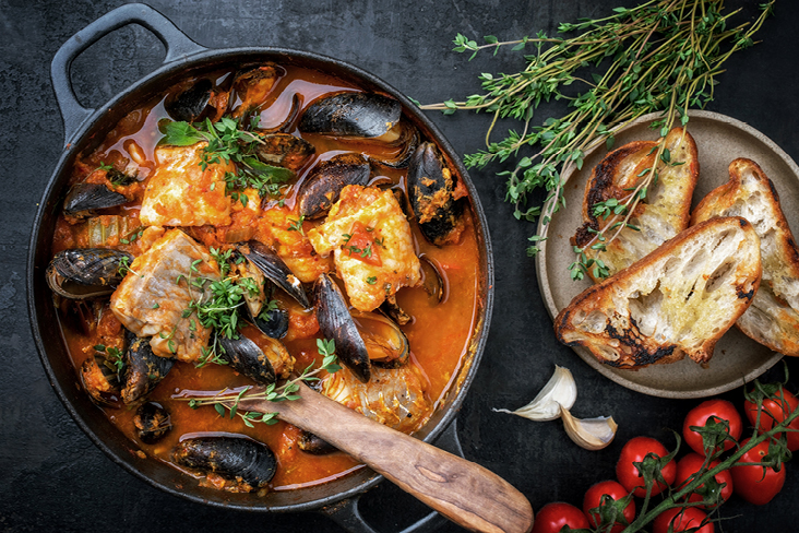 Poêle de ragoût de poisson et moules, servie avec du pain et des tomates juteuses.
