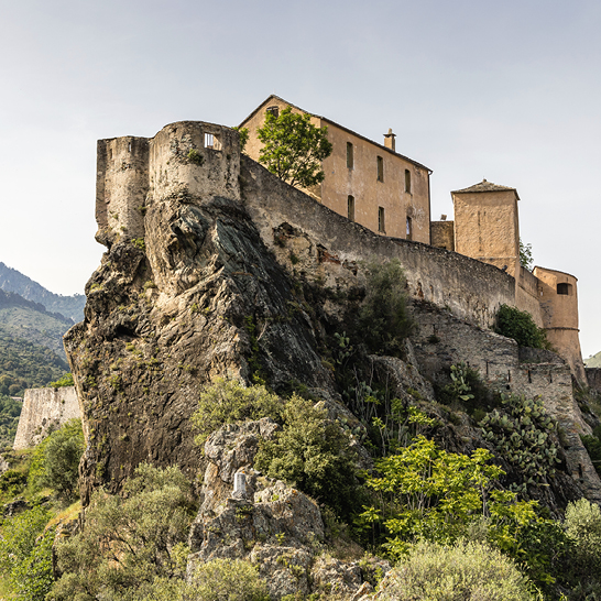 Bâtiment imposant perché sur une colline de rochers, avec un paysage naturel environnant.