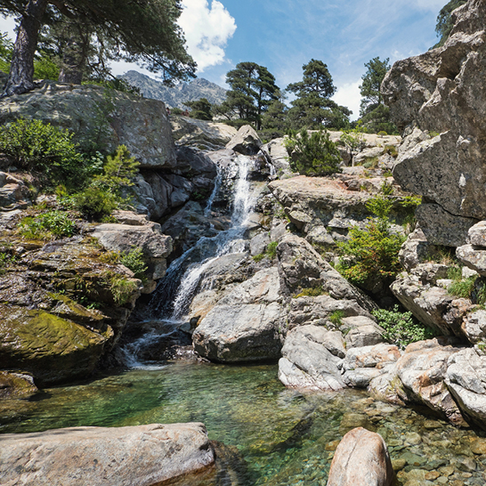 Une belle cascade entourée de montagnes, avec des rochers et des arbres en arrière-plan.