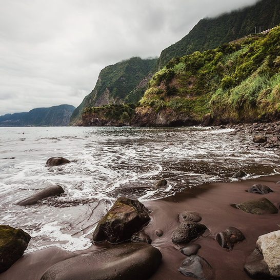 Ein Küstenabschnitt mit Felsen und Wasser, das ruhig am Strand entlang fließt.